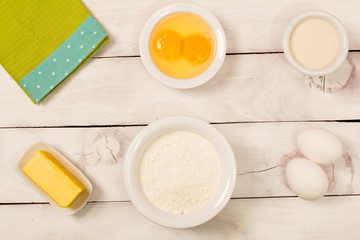 Baking in rustic kitchen (eggs, flour, milk, butter, sugar) on white  wooden table from above. 