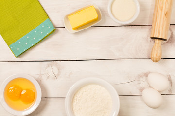 Baking in rustic kitchen ingredients (eggs, flour, milk, butter, sugar) on white  wooden table from above. 