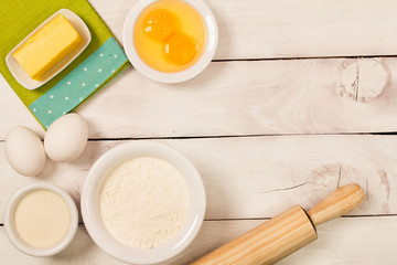 Baking in rustic kitchen recipe ingredients (eggs, flour, milk, butter, sugar) on white  wooden table from above. 