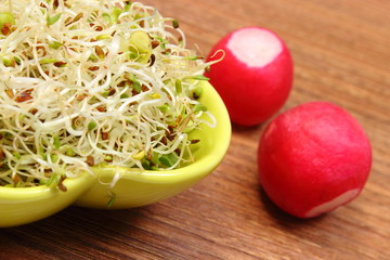 Bowl with alfalfa sprouts and radish on wooden table