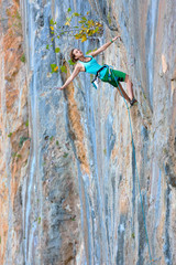 Young Female Rock Climber hanging on vertical natural Wall