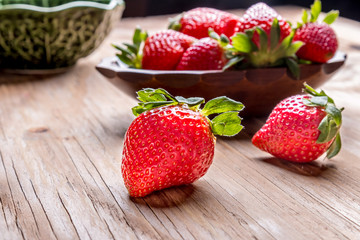 strawberries in a wooden bowl on the old wooden table and green