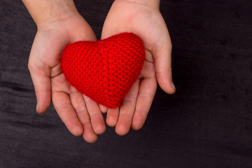 heart of red knitted crochet thread, in the children's hands