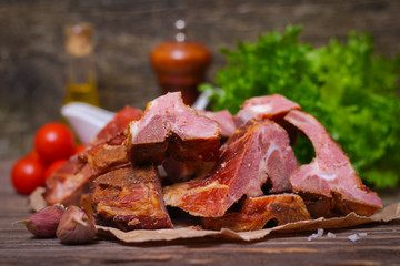 Smoked pork meat on the bone with vegetables on a wooden background. Snack for a beer or smoked broth.
