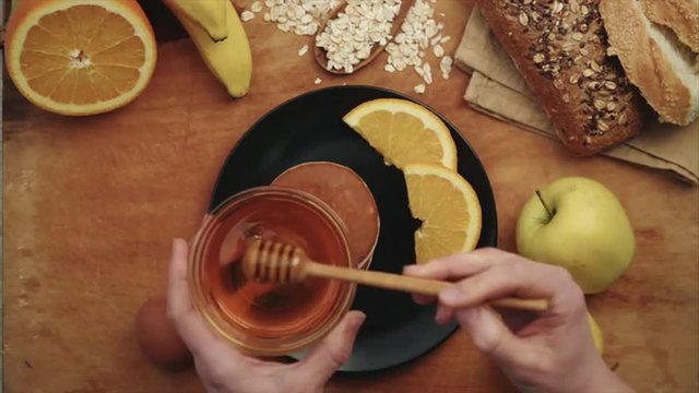 Young woman pouring bee honey with stick on pancakes. Fresh natural meal. Breakfast preparation. 