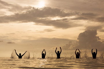 group of happy young people dancing and spraying at the beach on