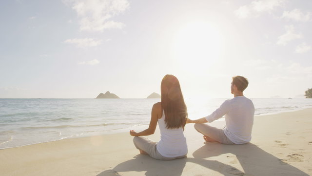 Yoga woman and man meditating in lotus pose relaxing outside on beach at sunrise. Couple woman and man in meditation in serene ocean landscape. Lanikai beach, Oahu, Hawaii, USA.