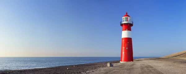 Fototapete Leuchtturm Rot-weißer Leuchtturm und ein strahlend blauer Himmel