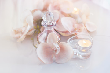Perfume or aromatic oil bottle surrounded by flowers and candles