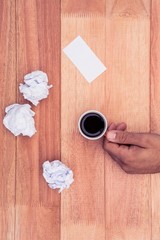 Cropped hand of businessman holding coffee cup by paper balls 