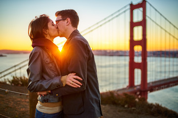 passionate kiss at sunrise in front of golden gate bridge with lens flare