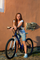 Young cute lady posing on a bike near the wall