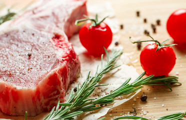 Pieces of crude meat with rosemary and tomatoes.