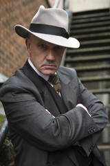 Vertical image of a mature man dressed as a 1940s gangster. looking into the camera.