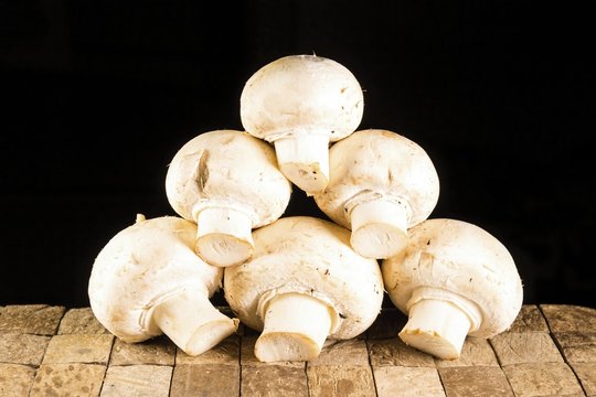 Many small raw unpeeled white champignons on brown wooden table. Macro shot.