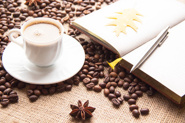 A cup of coffee, roasted coffee beans, notebook, pen and autumn