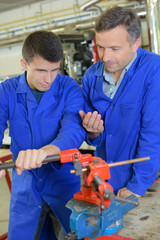 Tutor encouraging trainee to turn handle on equipment