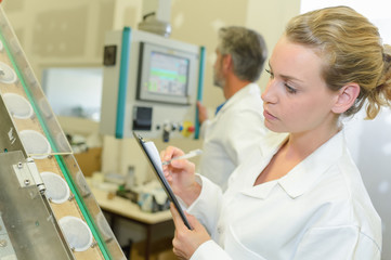Lady with clipboard inspecting row of beakers