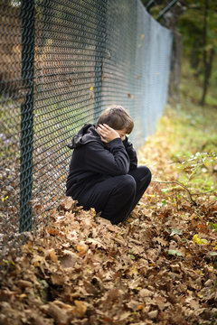 sad child sitting in front of a wire fence