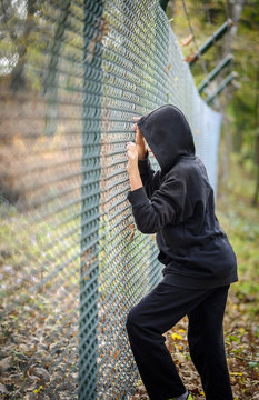 wire fence standing in front of hooded young