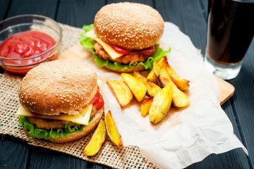 food, fast food, burgers with cheese , meat patty , lettuce, sauce , Baked potatoes and a drink , cola or beer on a wooden background