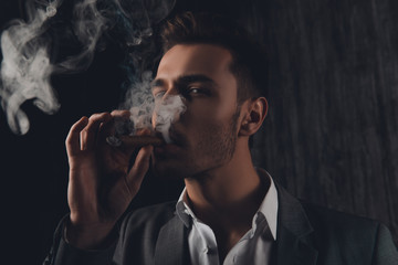 Cheeky man in suit on the grey background smoking a cigar
