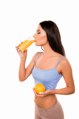 Slim young woman drinking orange juice and holding orange