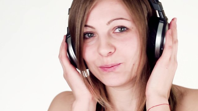 Beautiful and cheerful girl listening to music with headphones, dancing and looking at the camera