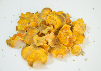 A pile of homemade baked sweet potato chips stacked over. A healthy sweetpotato vegetarian crisp snack seasoned with oregano and olive oil, isolated against white background.