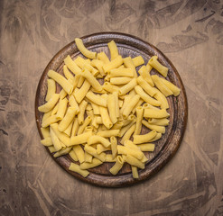 raw penne pasta on a round cutting board on wooden rustic background top view close up