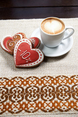 Cup of a perfection. High angle shot of a cup of coffee with froth design and three glazed red Valentine’s day cookies on the table