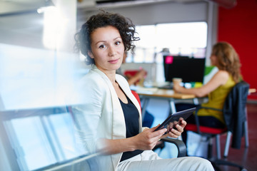 Confident female designer working on a digital tablet in red creative office space