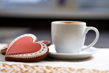 Fototapeta na wymiar Tasty offer. Closeup shot of a cup of warm beverage and a red heart shaped discount cookie on the cafe table