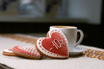 Thinking of you. Cup of cappuccino on the table and three heart shaped red cookies