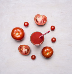 Fresh tomato juice in a glass with a straw, spread out around the sliced tomatoes on wooden rustic background top view close up