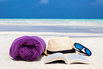 Handtuch, Hut, Buch und Sonnenbrille am Strand