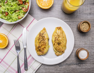 two fried chicken breasts with curry, fresh orange juice, fresh salad nutrition for athletes on wooden rustic background top view close up
