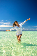 Young slim woman playing in the clean sea water making airplane wings under deep blue sky. Summer...