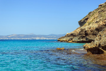 Fototapeta na wymiar Blue and clear water at Cap Enderrocat, Llucmajor rocky coast, bay of Palma de Mallorca and Serra de Tramuntana mountains in background horizon