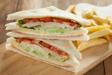 homemade club sandwich with french fries on wooden board