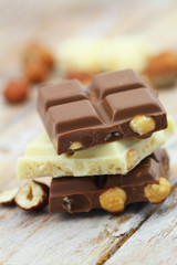Milk and white chocolate pieces with whole hazelnuts stacked up on wooden surface
