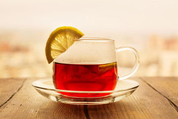 Black tea with lemon slices in a glass cup. View over window on city roofs. Toned image. Selective focus