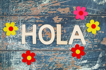 Hola (Hello in Spanish) written with wooden letters on rustic surface and colorful flowers
