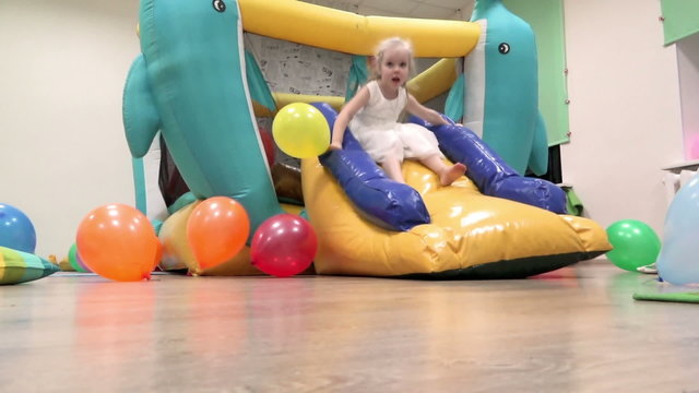 Girl riding a yellow slides on the big trampoline in a fabulous room
