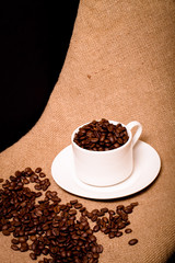 Cup, saucer and coffee beans on a burlap background. Toned
