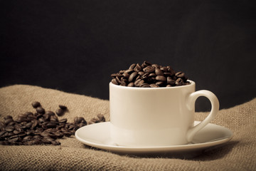 Cup, saucer and coffee beans on a burlap background. Selective f