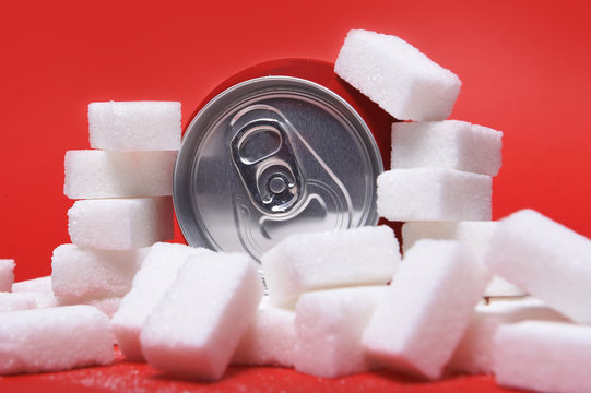 Cola Refreshing Drink Can And Lot Of White Sugar Cubes Representing The Big Amount Of Calories