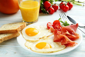 Fried eggs with bacon and toasts on plate on blue wooden table