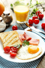 Fried eggs with bacon and toasts on plate on grey wooden table