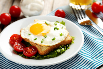 Fried eggs with toasts on plate on grey wooden table